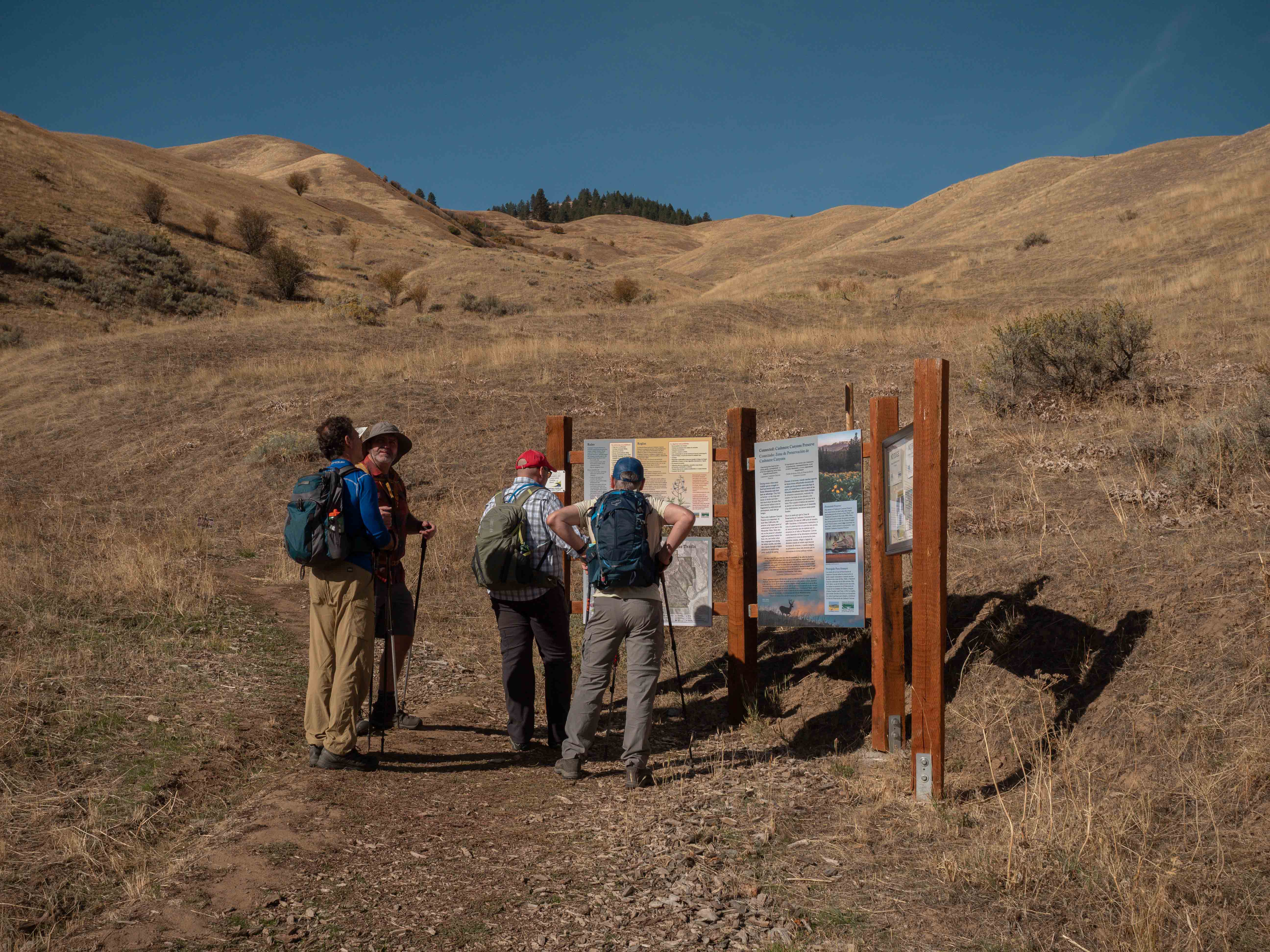 Three hikers gathered at the Cashmere Canyon trailhead information board, ponderosa pines in the background