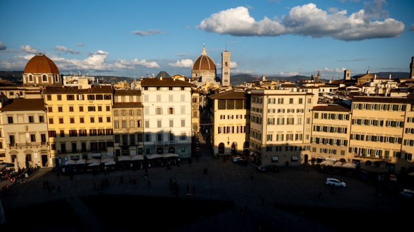 Elevated view over a Florence piazza with the Duomo rising above the rooftops, late afternoon light