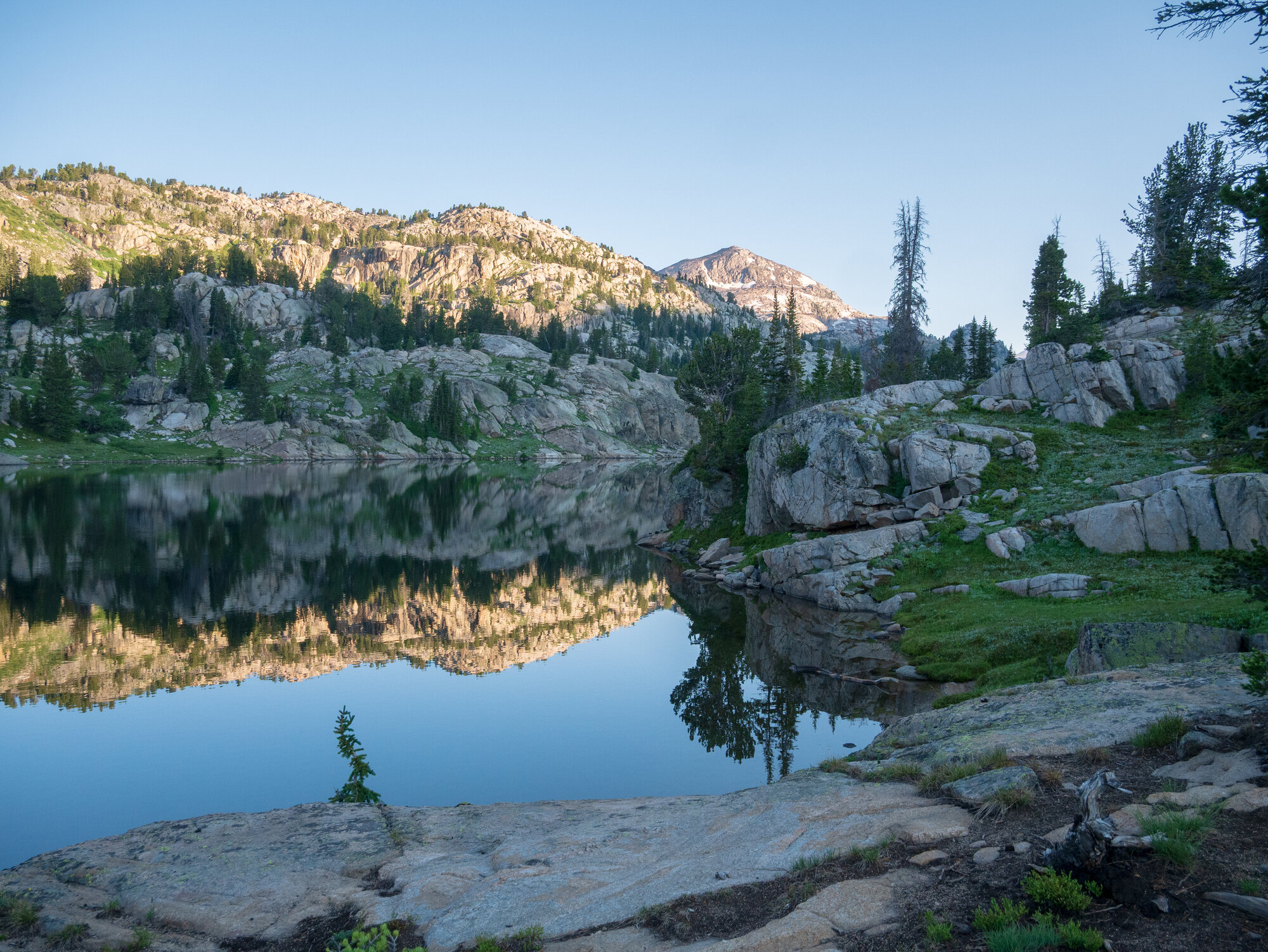 Becker Lake at first light, golden granite peaks and forested ridgeline reflected perfectly in the glassy still water